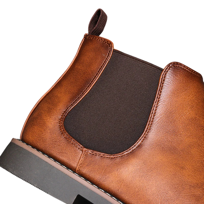 Zbliżenie na Arkadya Outlet Botki męskie wsuwane sztyblety zimowe zamknięta forma z brązowej skóry z ciemnym elastycznym panelem bocznym, widocznymi szwami, zakładką, czarną podeszwą i bez zapięcia, sfotografowane na jasnym tle.