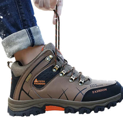 Osoba ubrana w Arkadya Outlet męskie buty wodoodporna konstrukcja ergonomiczna podeszwa z pomarańczowymi akcentami stąpa po śniegu, wiążąc sznurówki. Dżinsy mają mankiety, a ergonomiczne buty otaczają płatki śniegu.