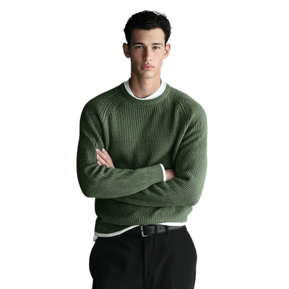 Młody mężczyzna o krótkich ciemnych włosach stoi ze skrzyżowanymi ramionami, ubrany w męski dekolt Arkadya Outlet okrągły prążkowana dzianina standardowy krój na białej koszuli i czarnych spodniach, na białym tle.