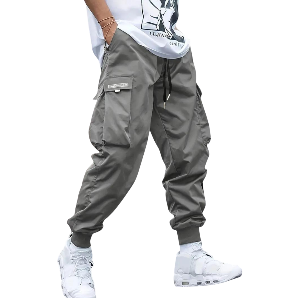 Osoba ubrana w Arkadya Outlet Męskie spodnie cargo | Dopasowana nogawka z wieloma kieszeniami, białe trampki i biały t-shirt z grafiką stoi na jednolitym jasnoszarym tle.