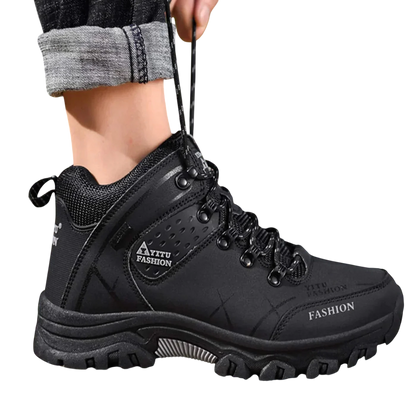 Mężczyzna w Arkadia Outlet Męskie buty wodoodporna konstrukcja ergonomiczna podeszwa stoi na skałach na zewnątrz. Czarne, sznurowane buty z grubą podeszwą i podwinięte jeansy to idealne buty do codziennego użytkowania.