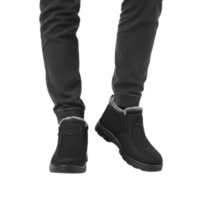 Osoba ubrana w Arkadya Outlet Męskie buty wodoodporne antypoślizgowe zimowe obuwie, z podszewką ze sztucznego futra i zamkiem błyskawicznym, w połączeniu z czarnymi spodniami, stoi na białym tle.