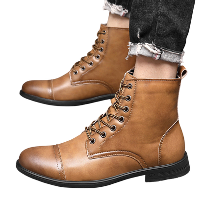 Osoba ubrana w czarne jeansy z postrzępionymi obszyciami i Arkadya Outlet Buty męskie wysoka cholewka z wiązaniem pełna wysokość w kolorze jasnobrązowym stoi na szarej podłodze wyłożonej kafelkami. Buty mają zaokrąglony nosek i widoczne szwy.