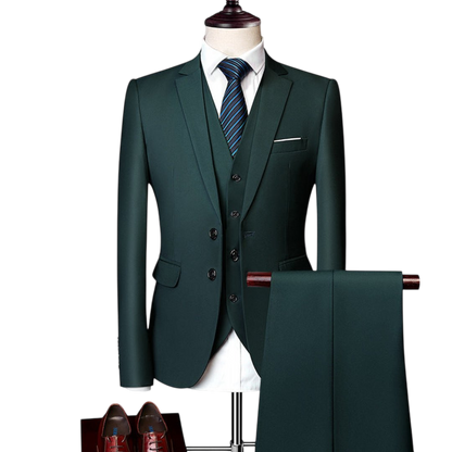 Komplet trzyczęściowy męski Arkadya Outlet: ciemnozielony dopasowany zestaw z marynarką, kamizelką i spodniami, do tego biała koszula, niebieski krawat w paski i brązowe buty podkreślające całość.