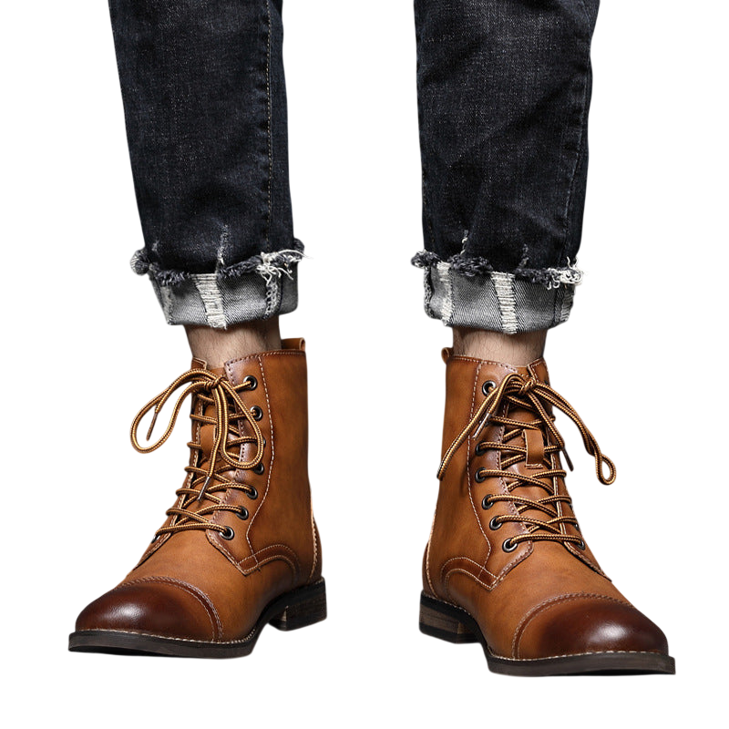 Osoba w podwiniętych ciemnych dżinsach i Arkadya Outlet Buty męskie wysoka cholewka z wiązaniem pełna wysokość stoi na wyłożonej kafelkami podłodze przy szarej ścianie.