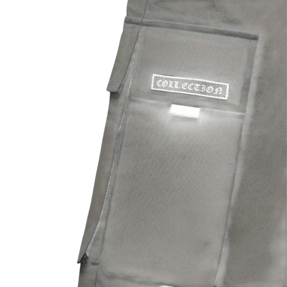 Zbliżenie na szarą kieszeń cargo z klapką i białą metką "COLLECTION" na męskim spodnie cargo marki Arkadya Outlet; posiada białą zakładkę pod metką i znajduje się na jednolitym jasnoszarym tle.