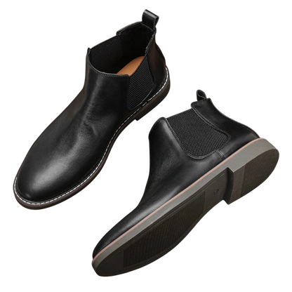 Arkadya Outlet Botki męskie wsuwane sztyblety zimowe zamknięta forma wykonane z czarnej skóry, z elastycznymi panelami, uchwytami z tyłu i gumową podeszwą z brązowym akcentem, prezentowane na białym tle.