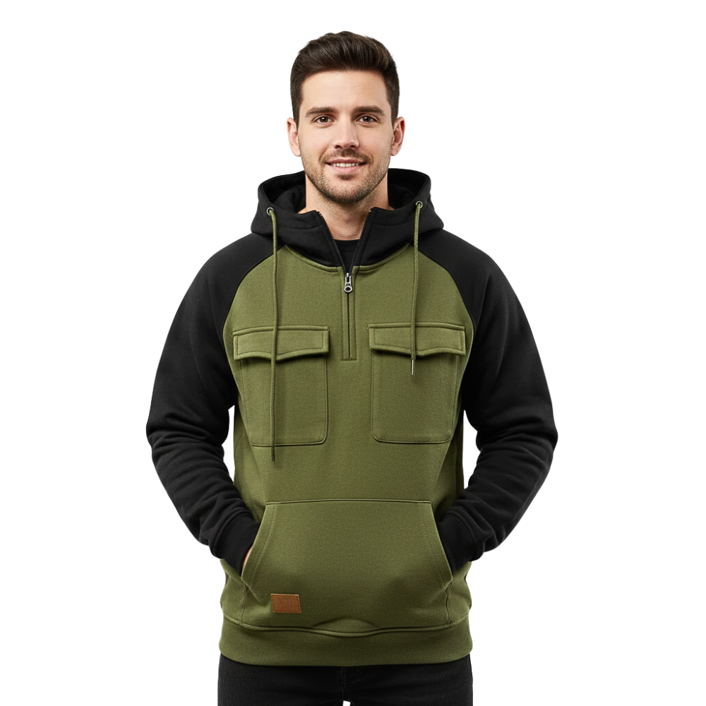 Mężczyzna o krótkich ciemnych włosach i lekkim uśmiechu stoi przodem do kierunku jazdy, ubrany w Arkadya Outlet Bluza męska dwukolorowa z kapturem i kieszeniami z przodu, z rękami w przednich kieszeniach.