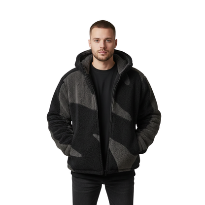 Mężczyzna z krótkimi włosami i brodą nosi czarno-szarą Kurtkę Z Kapturem Męska Luźny Krój Z Zamkiem Regulowana Dołem marki Arkadya Outlet na czarnej koszuli i spodniach, stojąc na prostym białym tle z rękami w kieszeniach.