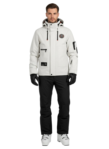 Mężczyzna stoi przodem do kierunku jazdy w Kurtce Zewnętrznej Męskiej Wodoodpornej Zapięcie na Zamek by Arkadya Outlet z czarnymi rękawiczkami, czarnymi spodniami, białymi butami narciarskimi, wieloma kieszeniami, naszywką na piersi i zwykłym białym tłem.