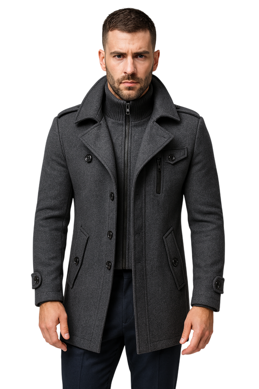 Mężczyzna z krótkimi włosami i brodą ma na sobie Męski Płaszcz by Arkadya Outlet - jesienno-zimowy płaszcz z długim rękawem w kolorze ciemnoszarym na zapinanym na zamek swetrze, stojący na jasnoszarym tle z poważną miną.