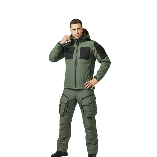 Mężczyzna pozuje pewnie na białym tle, ubrany w Arkadya Outlet zestaw odzieży outdoorowej męska kurtka i spodnie wodoodporne w kolorze oliwkowo-zielonym z czarnymi naszywkami, jedną rękę trzyma na biodrze, a drugą dotyka kaptura.