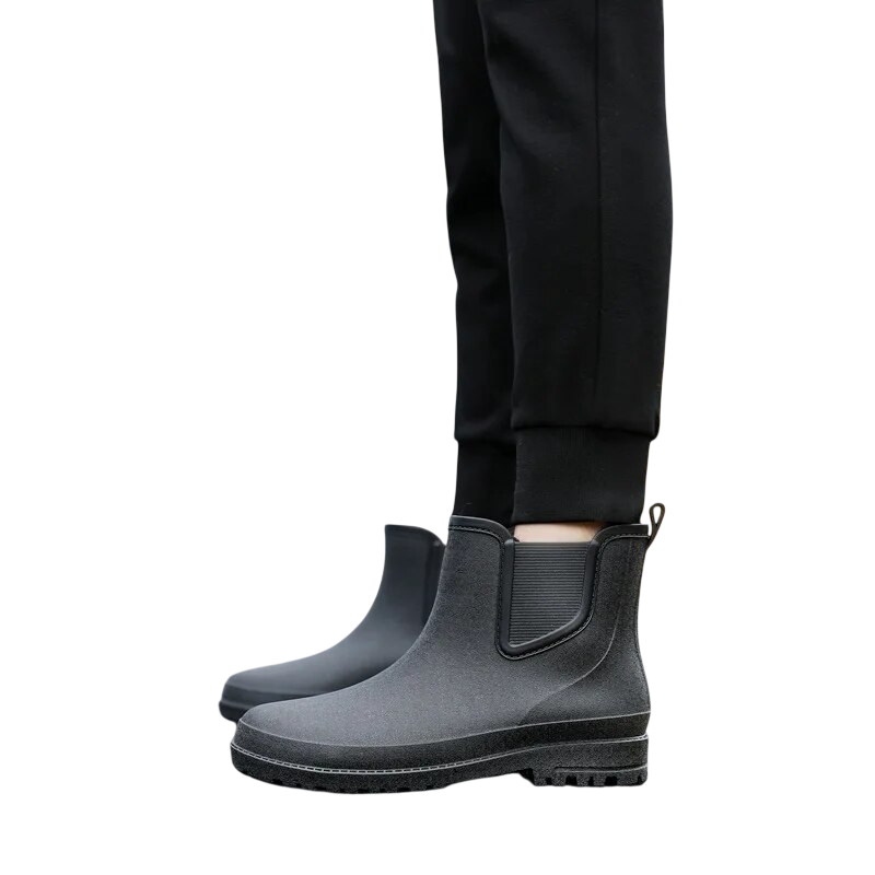 Osoba w czarnych spodniach modeluje Arkadya Outlet Buty Chelsea męskie zimowe wsuwane antypoślizgowe, stojąc na jasnym tle i prezentując widok obuwia z boku.