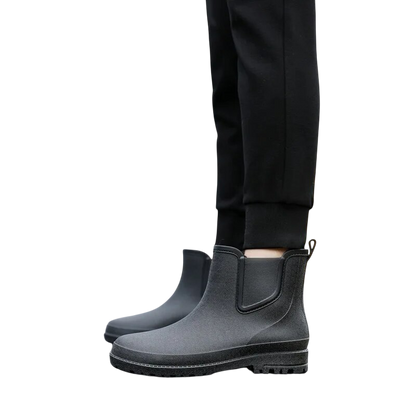 Osoba w czarnych spodniach modeluje Arkadya Outlet Buty Chelsea męskie zimowe wsuwane antypoślizgowe, stojąc na jasnym tle i prezentując widok obuwia z boku.