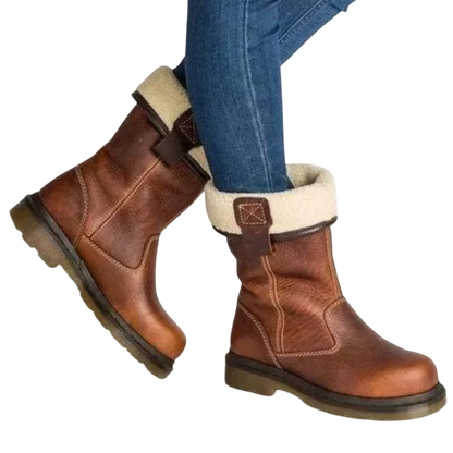 Osoba nosi niebieskie dżinsy i Arkadya Outlet Buty za kostkę męskie wsuwane z okrągłym noskiem i podeszwą, z solidnymi podeszwami i lekką futrzaną podszewką, z wierzchami złożonymi, aby odsłonić przytulne wnętrze na jednolitym tle.