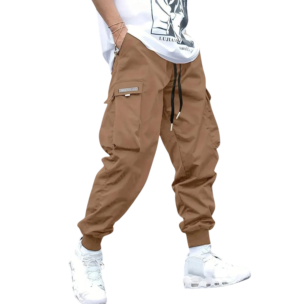 Osoba modeluje Arkadya Outlet Spodnie cargo męskie dopasowana nogawka z wieloma kieszeniami, w połączeniu z białą graficzną koszulką i białymi trampkami, na jednolitym szarym tle. Twarz nie jest widoczna.