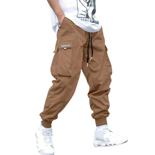 Osoba modeluje Arkadya Outlet Spodnie cargo męskie dopasowana nogawka z wieloma kieszeniami, w połączeniu z białą graficzną koszulką i białymi trampkami, na jednolitym szarym tle. Twarz nie jest widoczna.