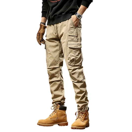 Mężczyzna w Arkadia Outlet Spodnie cargo męskie taktyczne wielokieszeniowa konstrukcja, brązowe buty robocze, czarna koszula z długim rękawem, zegarek i brązowe rękawiczki stoi na prostym białym tle.