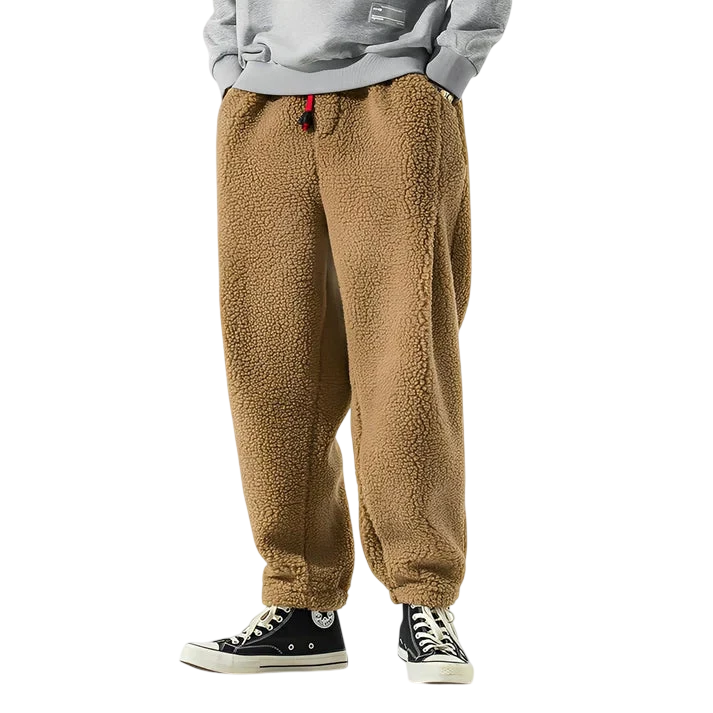 Model (głowa niewidoczna) stoi na prostym białym tle ubrany w Spodnie Męskie Luźny Krój Elastyczny Pas Do Domu I Wypoczynku by Arkadya Outlet, w połączeniu z szarą bluzą i czarnymi sneakersami z wysokim stanem. Ręce w kieszeniach.