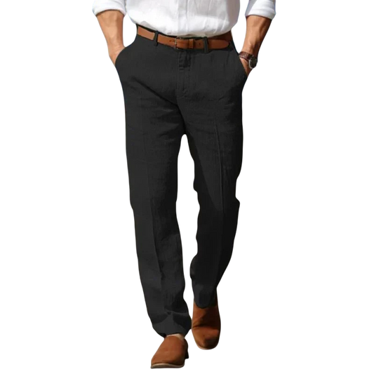 Mężczyzna w białej koszuli, brązowym pasku, Arkadya Outlet Spodnie męskie luźny krój pełna długość do codziennego noszenia i brązowych butach idzie piaszczystą ścieżką plaży z rękami w kieszeniach i oceanem za sobą.