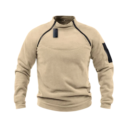 Beżowa bluza męska polarowa Arkadya Outlet z długim rękawem, wysokim kołnierzem, zamkami na froncie i ramieniu oraz kieszenią na lewym rękawie, prezentowana na tle rozmytych gór.