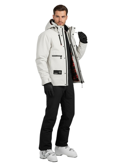 Mężczyzna ubrany w kurtkę Zewnętrzna Męska Wodoodporna z zapięciem na zamek, czarne rękawiczki, czarne spodnie i białe buty narciarskie stoi przodem do kierunku jazdy. Kurtka jest częściowo rozpięta, aby pokazać czerwono-czarną podszewkę w kratę.