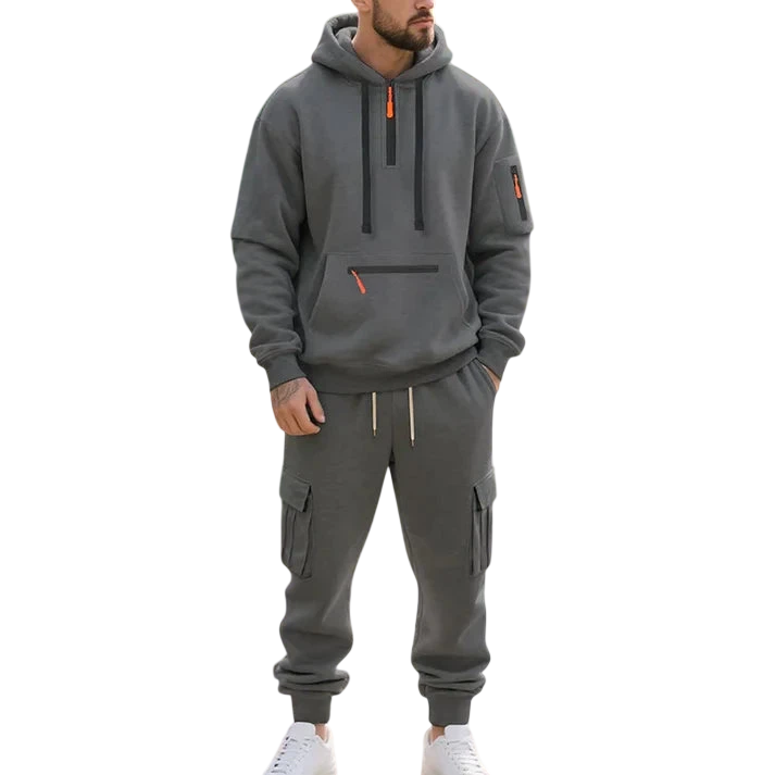 Mężczyzna w szarej bluzie z kapturem z zamkiem i spodniach dresowych cargo z outletu Arkadya Męski dres wyściełane wnętrze dwuczęściowy komplet stoi nad stawem z liliami, pomarańczowymi rybkami koi, zieloną trawą i drzewami.