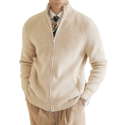 Mężczyzna nosi Arkadya Outlet Kardigan męski zapinany na zamek błyskawiczny dopasowany krój w kolorze beżowym na białej koszuli i wzorzystym krawacie, z brązowymi spodniami i zegarkiem na rękę, ręce w kieszeniach.