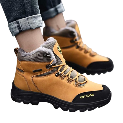 Osoba nosi Arkadya Outlet Buty zimowe outdoor męskie wiązane z antypoślizgową podeszwą z podszewką ze sztucznego futra i napisem "OUTDOOR" z boku. Chropowata podeszwa zapewnia przyczepność. Dżinsy są podwinięte przy kostkach.