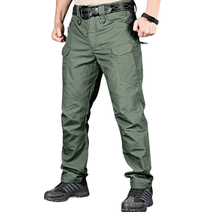 Osoba ubrana w spodnie Arkadya Outlet cargo męskie krój slim z wieloma kieszeniami użytkowymi, czarny pasek, czarny zegarek i czarne buty sportowe stoi na jednolitym szarym tle z zaciśniętymi pięściami i lekko zgiętymi ramionami.