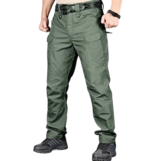 Osoba ubrana w spodnie Arkadya Outlet cargo męskie krój slim z wieloma kieszeniami użytkowymi, czarny pasek, czarny zegarek i czarne buty sportowe stoi na jednolitym szarym tle z zaciśniętymi pięściami i lekko zgiętymi ramionami.