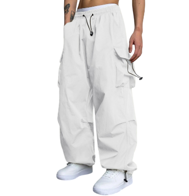 Osoba ubrana w cargo Męskie Spodnie Arkadya Outlet z szeroką nogawką i wieloma kieszeniami, w połączeniu z białymi sneakersami, stoi w pomieszczeniu na tle gładkiej ściany i ciemnej podłogi.