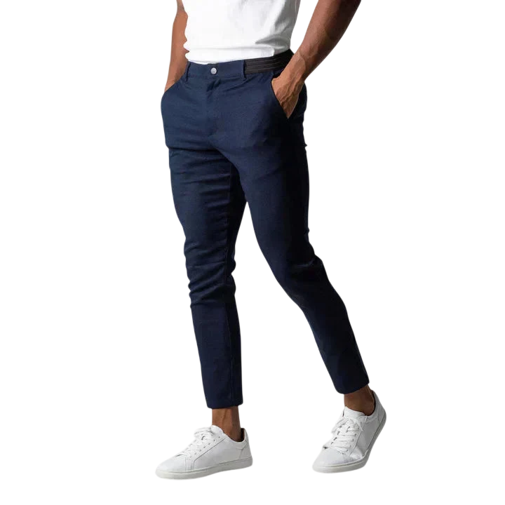 Osoba nosząca Arkadya Outlet Spodnie chinosy męskie o modnym kroju i pełnej długości, białą koszulkę i białe sneakersy stoi z rękami w kieszeniach na jasnoszarym tle. Głowa osoby nie jest widoczna na zdjęciu.