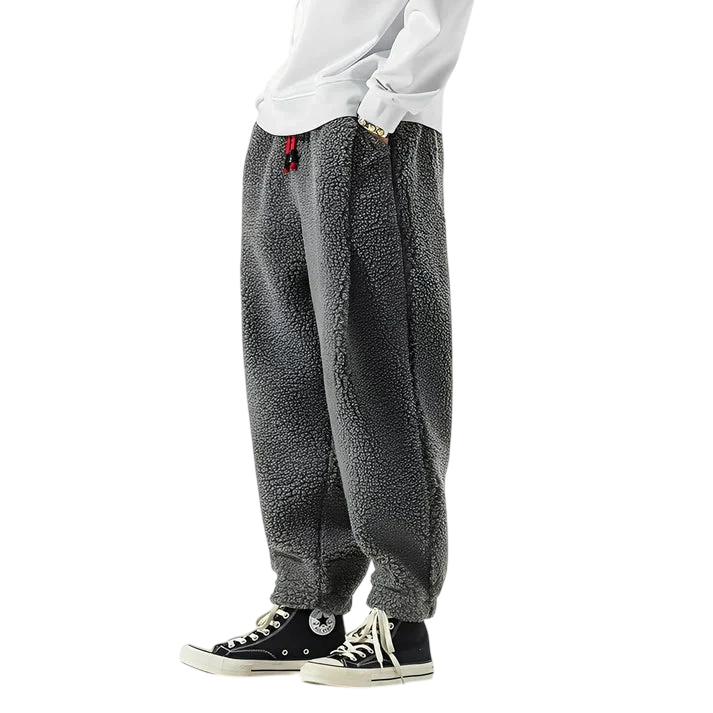 Osoba ma na sobie Arkadya Outlet Spodnie Męskie Luźny Krój Elastyczny Pas Do Domu I Wypoczynku, białą bluzę i czarne wysokie trampki Converse. Tylko dolna część ciała jest widoczna na białym tle.