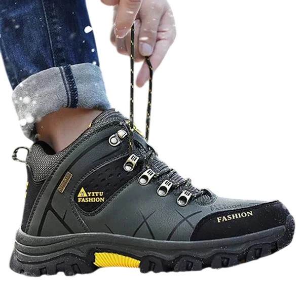 Osoba ubrana w ciemnozielone Arkadya Outlet męskie buty wodoodporna konstrukcja ergonomiczna podeszwa z żółtymi akcentami i napisem "FASHION" z boku stoi na zaśnieżonej ziemi, regulując sznurówki, gdy pada śnieg, a drzewa rozmywają się w tle.