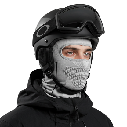 Osoba w odzieży zimowej, ubrana w Arkadya Outlet Kominiarka męska osłona głowy i szyi, czarny kask narciarski z goglami i czarną kurtkę patrzy przed siebie na prostym, jasnym tle.