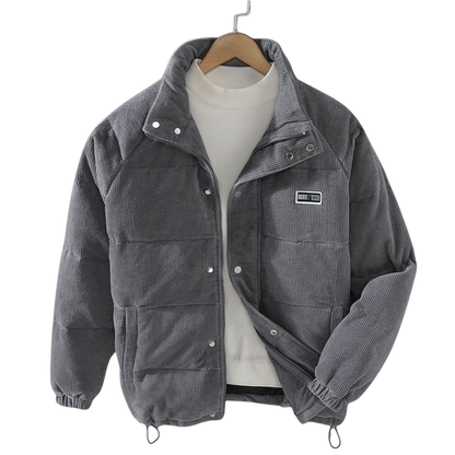 Arkadya Outlet Kurtka zimowa męska strukturalny krój z czystymi liniami, szara sztruksowa kurtka z guzikami zatrzaskowymi, wysokim kołnierzem i naszywką na piersi, jest prezentowana na wieszaku na białym golfie na jednolitym tle.