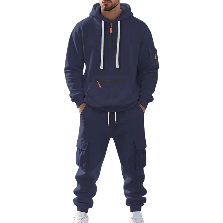 Osoba w granatowym Arkadya Outlet Męski dres wyściełane wnętrze dwuczęściowy komplet z zamkiem, z pasującymi cargo spodnie dresowe, stoi przy kamiennej fontannie w parku w słoneczny dzień. Twarz nie jest widoczna.