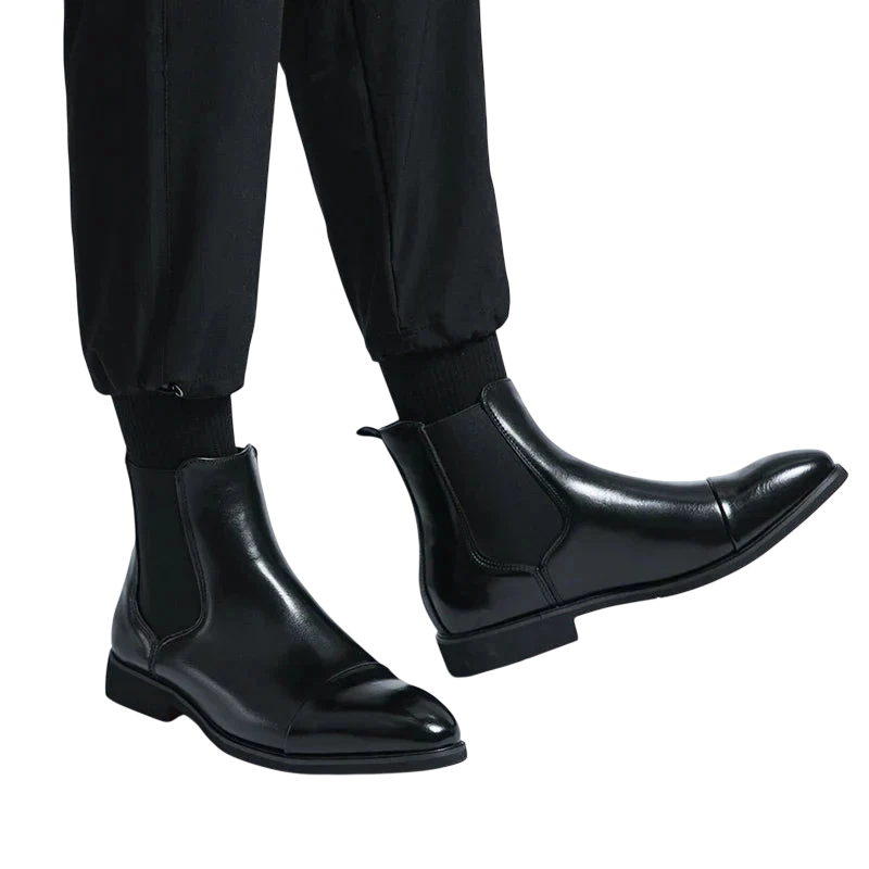 Osoba nosząca Arkadya Outlet Botki Chelsea Męskie Antypoślizgowa Zamknięta Konstrukcja w błyszczącej czerni z czarnymi spodniami, stojąca na prostym białym tle.