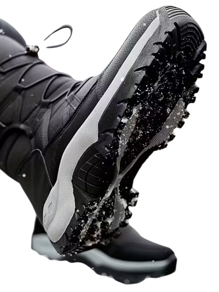 Zbliżenie pokazuje osobę ubraną w Arkadya Outlet Buty Śniegowe Męskie Wodoodporna Zimowa Konstrukcja Zewnętrzna z grubymi, chropowatymi podeszwami stąpającą po zaśnieżonej ziemi. Śnieg przylega do butów, pokazując ich przyczepność i zimową wytrzymałość.