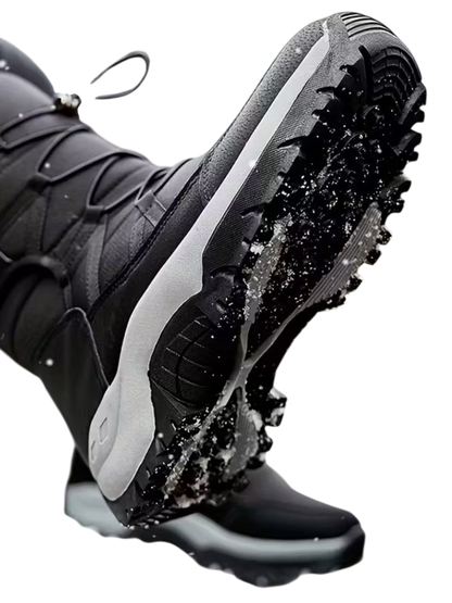 Zbliżenie pokazuje osobę ubraną w Arkadya Outlet Buty Śniegowe Męskie Wodoodporna Zimowa Konstrukcja Zewnętrzna z grubymi, chropowatymi podeszwami stąpającą po zaśnieżonej ziemi. Śnieg przylega do butów, pokazując ich przyczepność i zimową wytrzymałość.