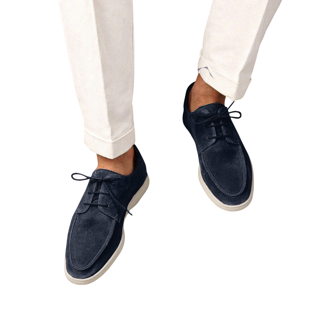 Osoba w białych spodniach z mankietami i Arkadya Outlet Buty Żeglarskie Męskie Sznurowane Niskie z gumową podeszwą w ciemnogranatowym kolorze z białymi podeszwami, stojąca na jasnoszarym tle.