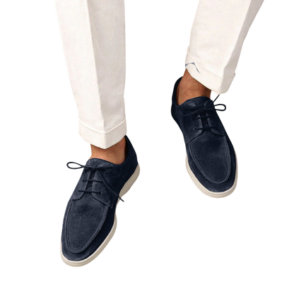 Osoba w białych spodniach z mankietami i Arkadya Outlet Buty Żeglarskie Męskie Sznurowane Niskie z gumową podeszwą w ciemnogranatowym kolorze z białymi podeszwami, stojąca na jasnoszarym tle.