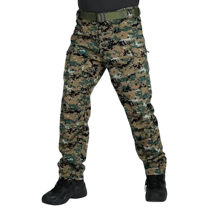 Osoba stoi z rozstawionymi nogami, ubrana w spodnie Arkadya Outlet cargo męskie krój slim z wieloma kieszeniami użytkowymi w kamuflażu cyfrowym, zielony pasek, czarne buty i ciemną koszulę. Zdjęcie jest przycięte powyżej talii na jednolitym jasnoszarym tle.