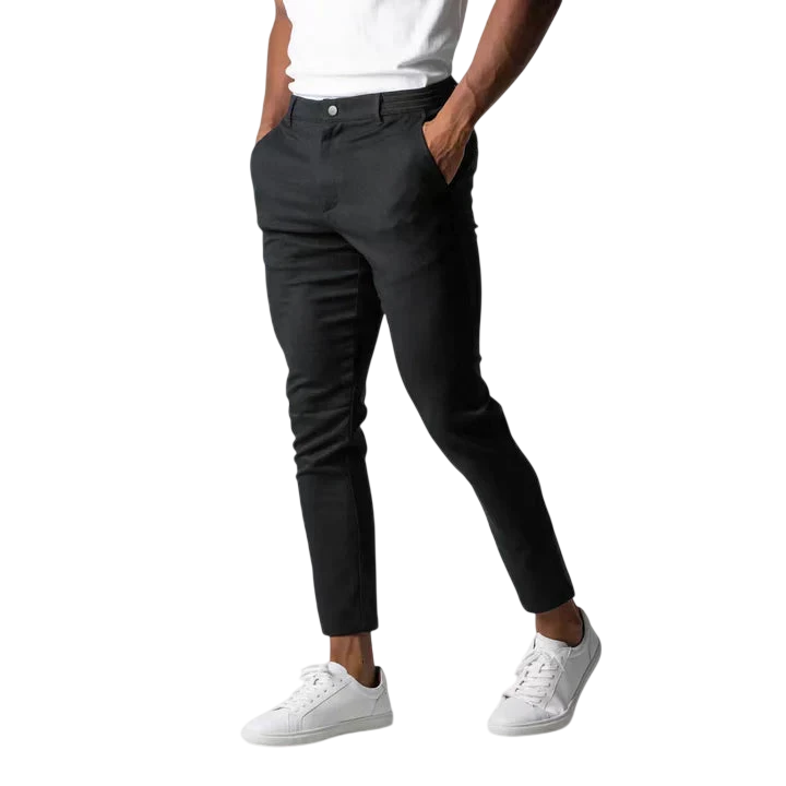 Osoba w białym t-shircie, Arkadya Outlet spodnie chinos męskie modny krój pełna długość użytkowy pas w czarnym slim-fit i białe trampki stoi z rękami w kieszeniach na jednolitym szarym tle; górna część ciała jest przycięta.