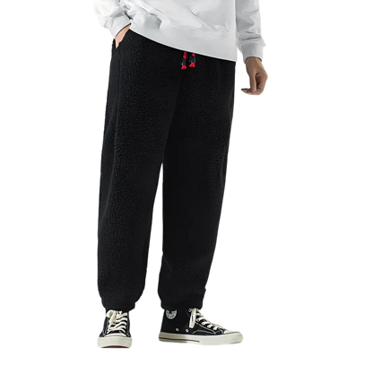 Osoba w Arkadia Outlet Spodnie Męskie Luźny Krój Elastyczny Pas Do Domu I Wypoczynku, z czerwonymi ściągaczami, białą bluzą i czarnymi high-topami z białymi podeszwami stoi na białym tle.