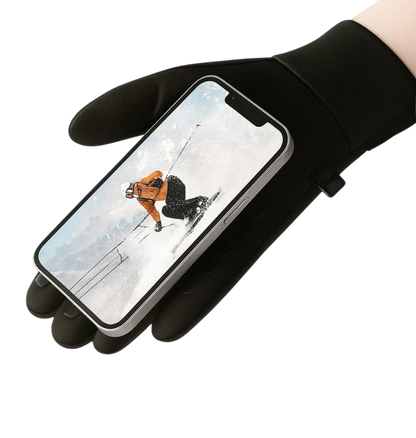Dłoń w czarnej rękawiczce, ubrana w Rękawice termiczne męskie wodoodporny uchwyt na chłód plenerowy Arkadya Outlet, trzyma smartfon przedstawiający narciarza. Rękawica posiada antypoślizgową fakturę oraz napis "ANTI-SLIP ONTWERP" ze znaczkiem powyżej.