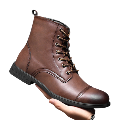 Osoba trzyma buty męskie Arkadya Outlet z pełną wysokością cholewki i wiązaniami, w brązowym kolorze ze złotymi oczkami i czarną podeszwą na tle szarym.