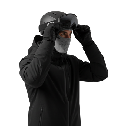 Osoba w odzieży zimowej - czarnej kurtce zimowej, rękawicach, kasku, goglach narciarskich i Arkadia Outlet Kominiarka męska osłona głowy i szyi do użytku zewnętrznego - dopasowuje gogle na jednolitym jasnoszarym tle.