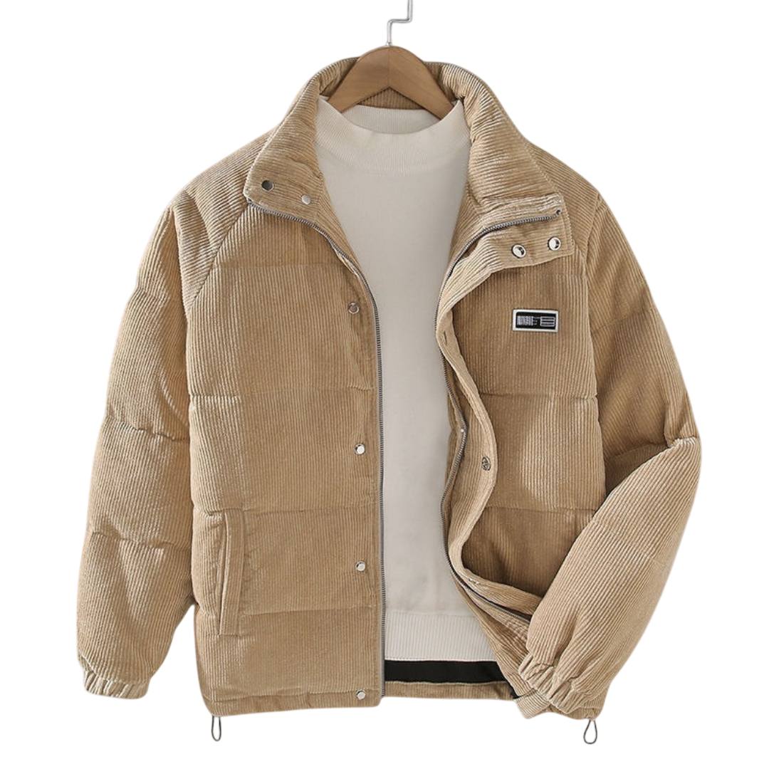 Kurtka zimowa męska strukturalny krój z czystymi liniami marki Arkadya Outlet to beżowa sztruksowa kurtka puchowa z guzikami zatrzaskowymi i wysokim kołnierzem, idealna do miejskich stylizacji, prezentowana na wieszaku na jasnym swetrze.